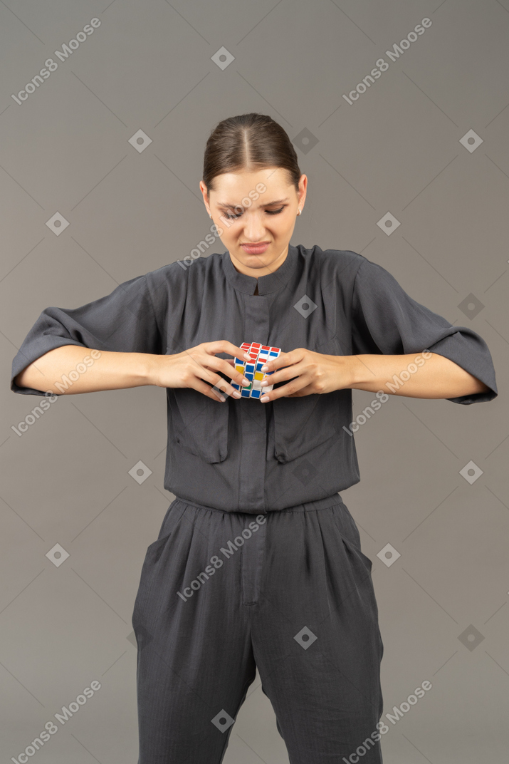 Front view of young woman in a jumpsuit trying to solve the rubik's cube puzzle