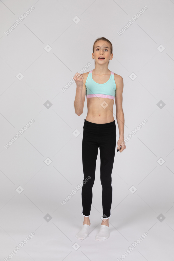 Vista frontal de uma adolescente emocional em roupas esportivas, levantando a mão e olhando para cima