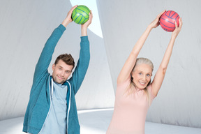 Old woman and young man making exercise and holding balls up above head