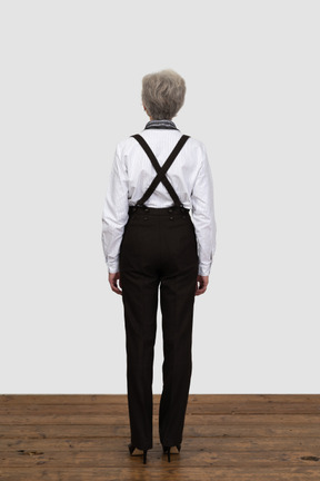 Back view of an old female with suspenders standing still in an empty room