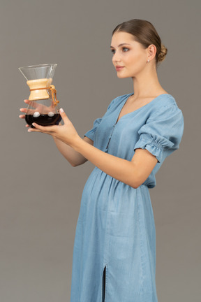 Vue de trois quarts d'une jeune femme en robe bleue tenant un pichet de vin