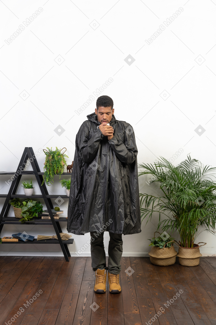 Homem de capa de chuva segurando um copo com os olhos fechados
