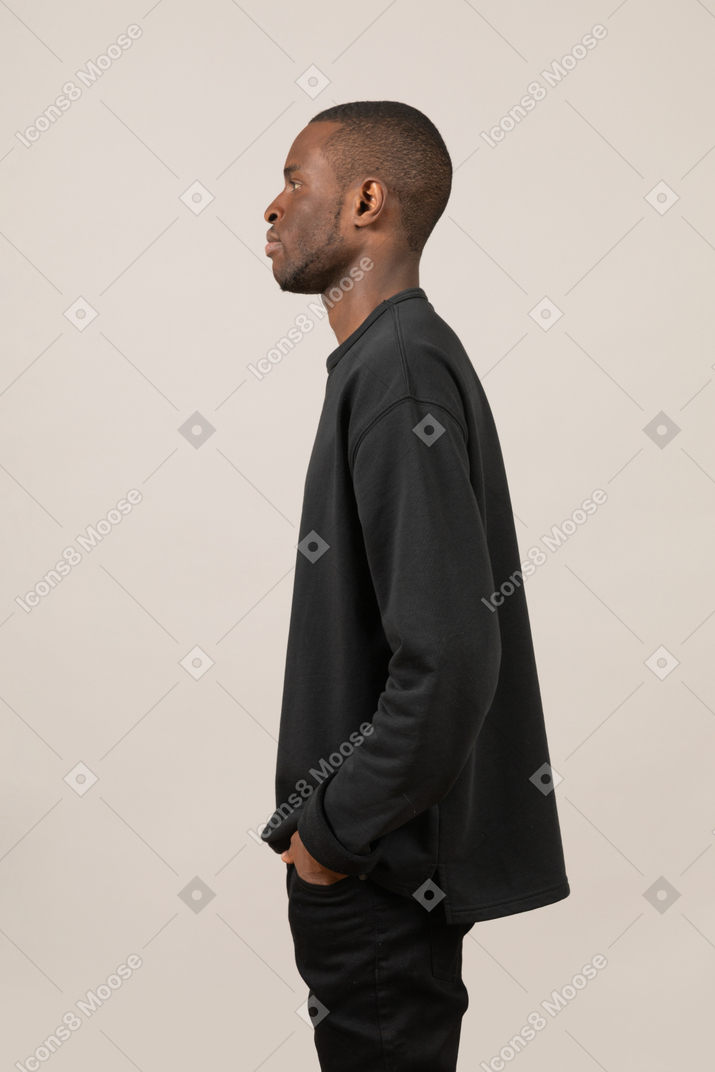 Side view of a young man standing with hands in pockets