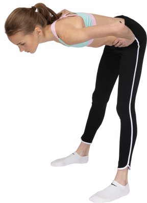 Vista de tres cuartos de una jovencita en ropa deportiva poniendo las manos en las caderas mientras se inclina hacia adelante