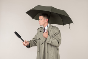 Serious looking male reporter holding microphone and standing under umbrella