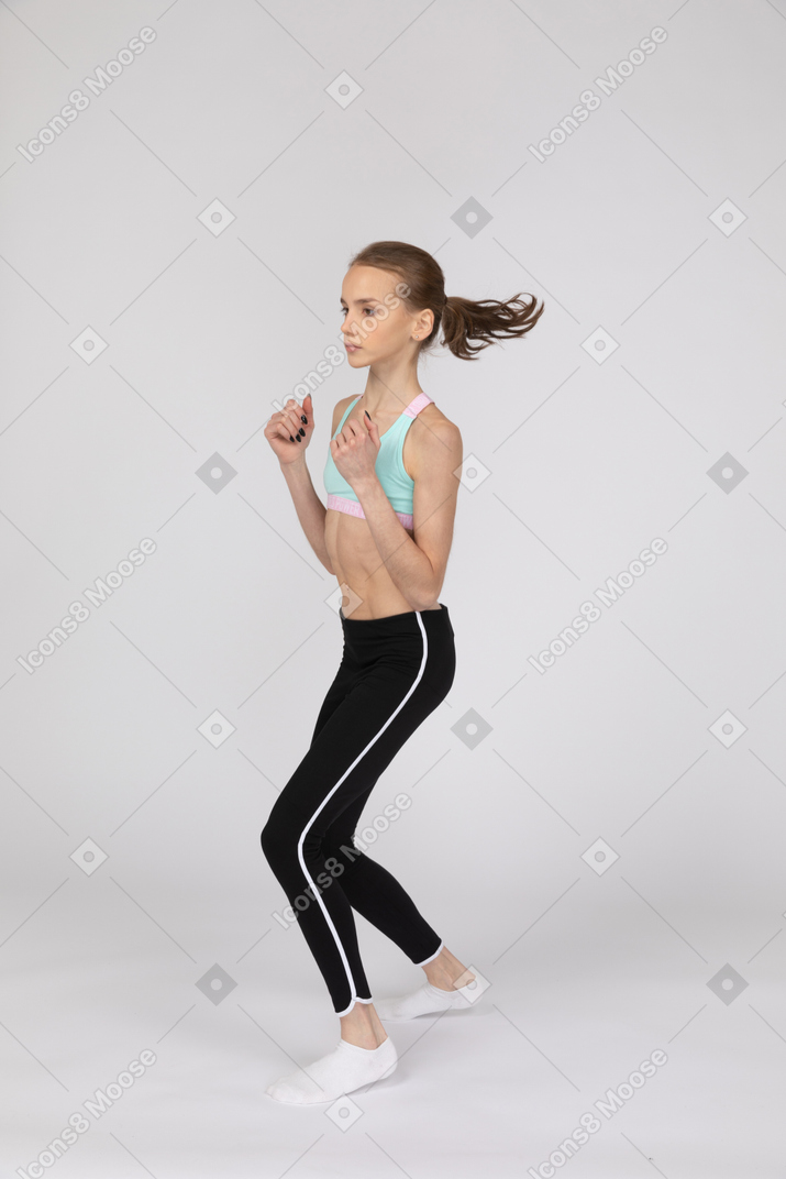 Vista de tres cuartos de una adolescente en ropa deportiva dando un paso adelante mientras aprieta los puños