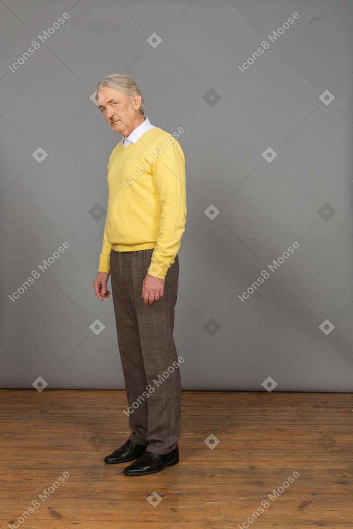 Three-quarter view of an old sad man in yellow pullover leaning forward and looking at camera