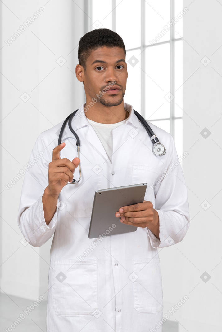 A man in a white lab coat pointing finger and holding a tablet