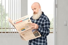 A bald man with a beard reading a newspaper