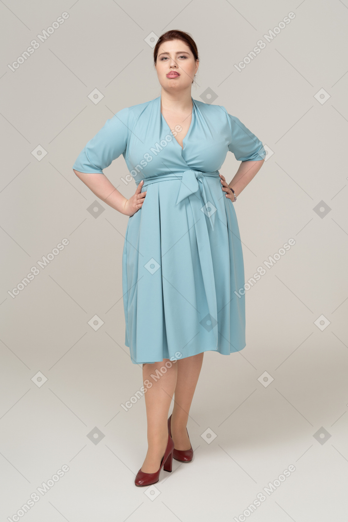 Vue de face d'une femme en robe bleue posant avec les mains sur les hanches et montrant la langue