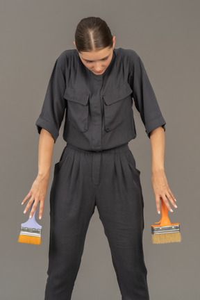 Woman in gray coveralls holding paint brushes