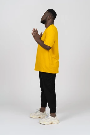Side view of a young dark-skinned man in yellow t-shirt holding hands together