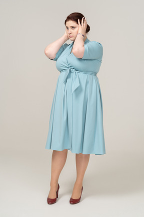 Вид сбоку на женщину в синем платье, закрывающую уши руками