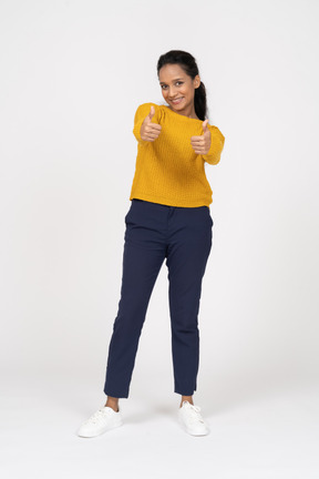 Front view of a happy girl in casual clothes showing thumbs up and looking at camera