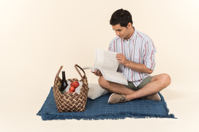 Young caucasian guy sitting on blanket and holding magazine opened