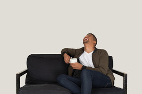 Front view of a smiling young man sitting on a sofa with a cup of coffee