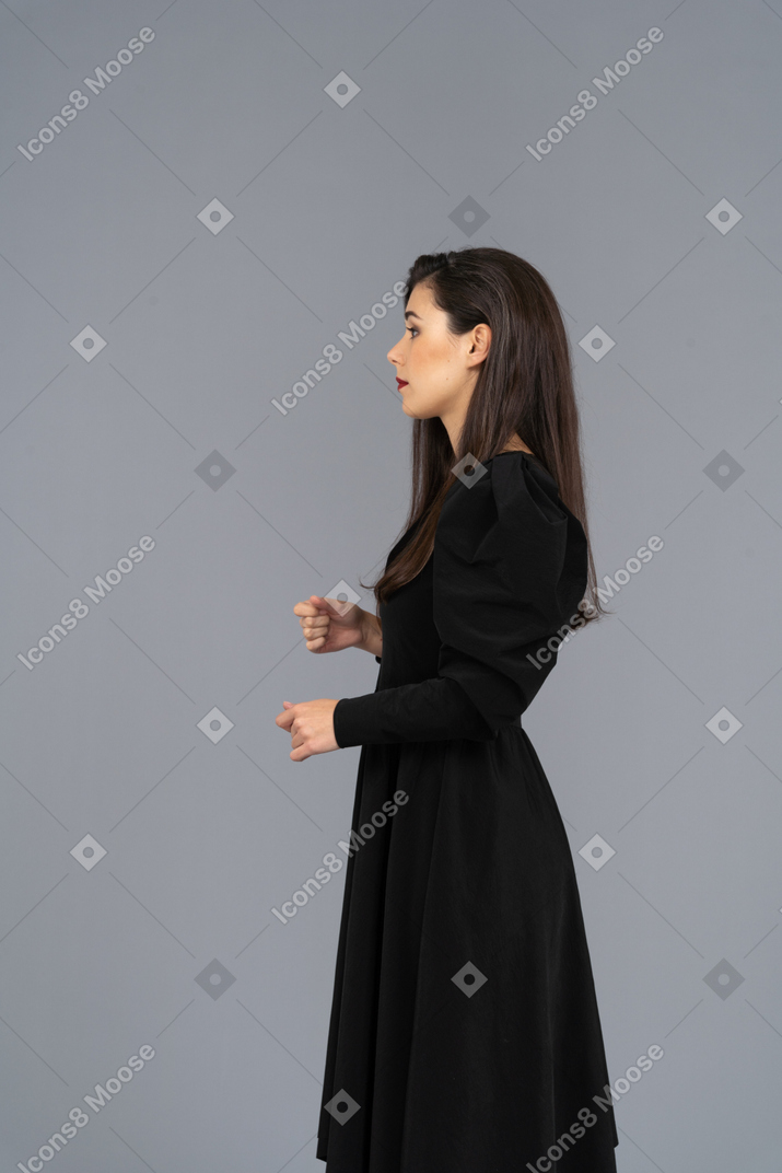 Vista lateral de uma jovem em um vestido preto levantando as mãos