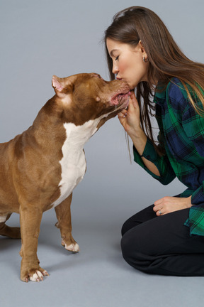 Close-up una mujer sentada y besando a su bulldog marrón