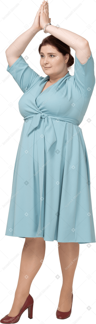 머리 위로 손을 들고 서 있는 파란 드레스를 입은 여자의 전면 보기