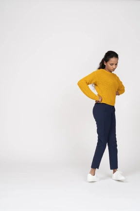 Side view of a girl in casual clothes posing with hands on hips and looking down