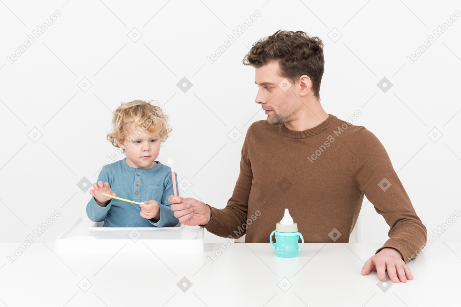 Отец учит своего маленького сына пользоваться ложкой