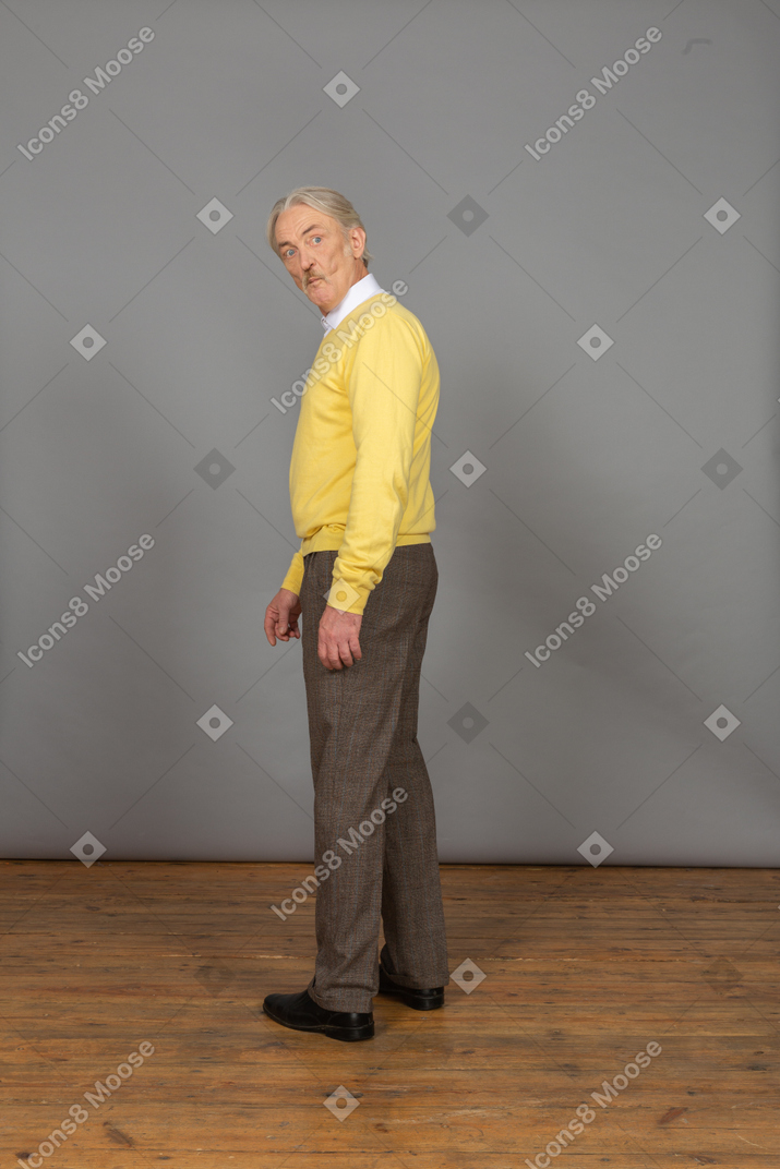 Side view of an old surprised man in yellow pullover bending down and looking at camera and grimacing