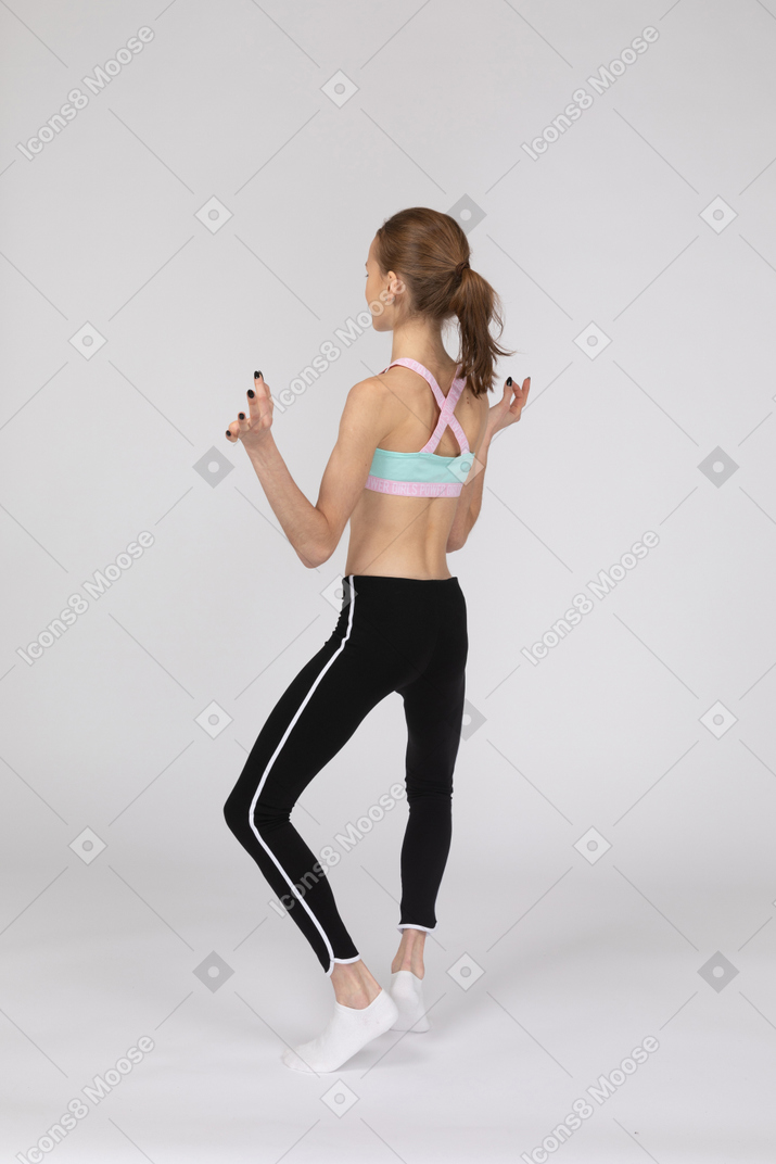 Vista traseira a três quartos de uma adolescente em roupas esportivas separando as pernas