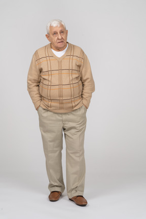 Front view of an old man in casual clothes standing with hands in pockets