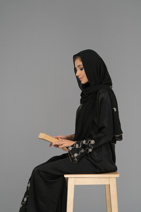 A covered arab woman holding a book on her knees