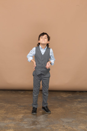Front view of a boy in grey suit posing with hand on hip and looking up
