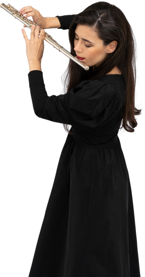 Vista di tre quarti di una giovane donna seria in abito nero che suona il flauto