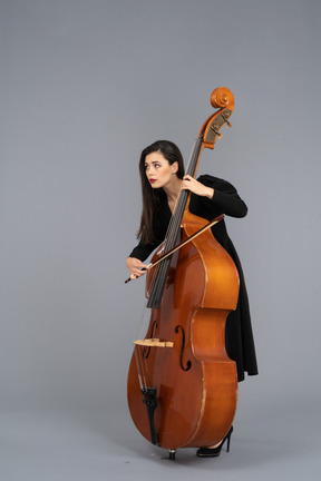 Three-quarter view of a young woman in black dress playing the double-bass with a bow