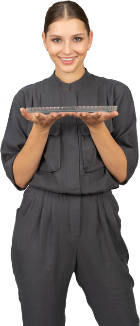 Вид спереди молодой женщины в комбинезоне, держащей стеклянную тарелку