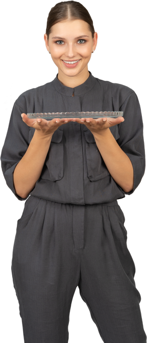 Front view of a young woman in a jumpsuit holding glass plate