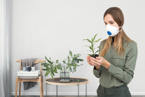 Mujer joven con máscara médica sosteniendo una planta en maceta