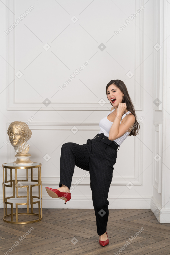 De cuerpo entero de una mujer joven enérgica pateando mientras está de pie cerca de la escultura griega dorada