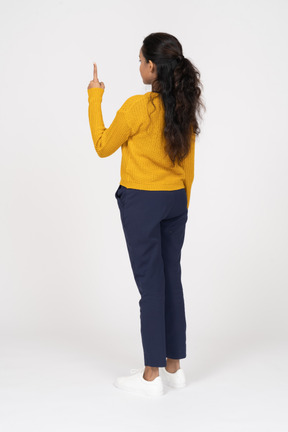 Vista traseira de uma garota com roupas casuais apontando para cima com um dedo