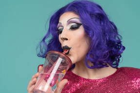 Primo piano di una drag queen che sorseggia un drink attraverso la paglia