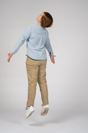 Back view of a boy jumping with his arms outstretched and looking up