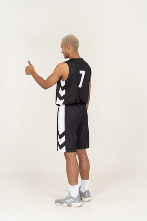 Three-quarter back view of a young male basketball player showing thumb up