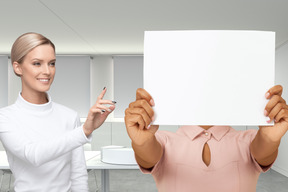 A woman holding up a paper sheet in front of her face and woman next to her pointing at it