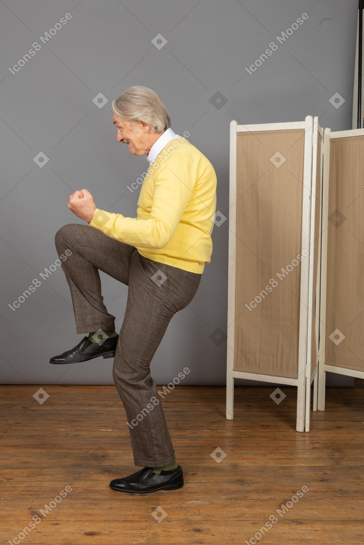 Side view of a happy old man clenching fists and raising his leg