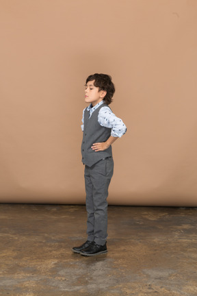 一个穿着西装、双手叉腰站着的可爱男孩的侧视图