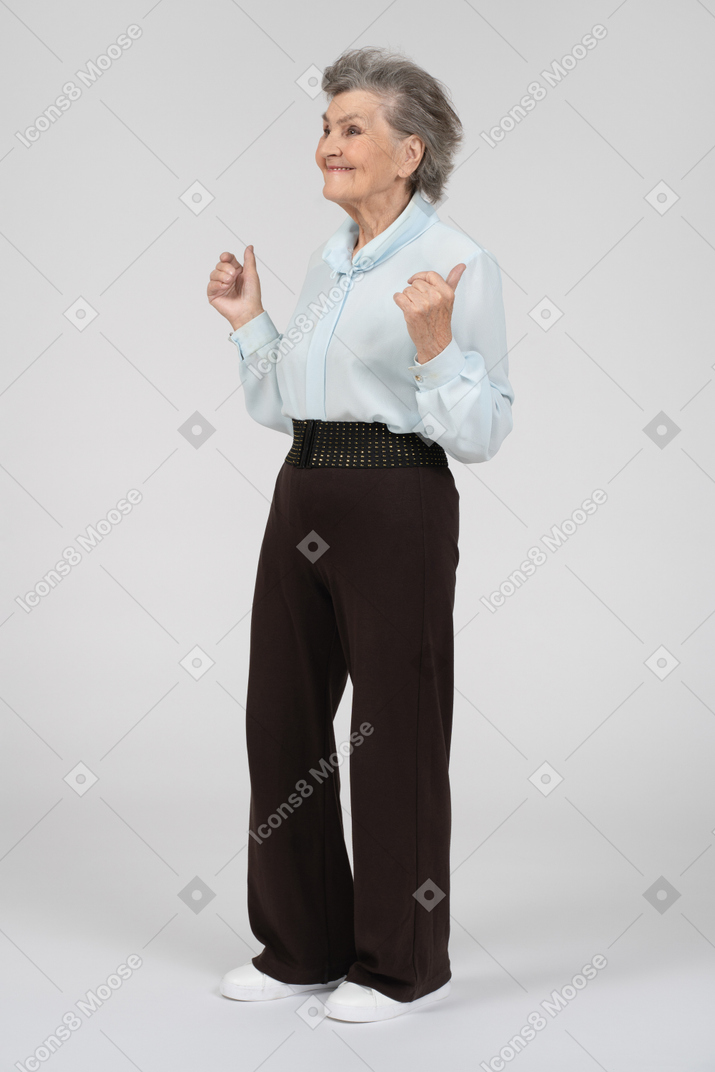 Вид в три четверти на пожилую женщину, улыбающуюся с поднятыми большими пальцами