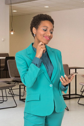 A woman in a turquoise suit looking at her cell phone