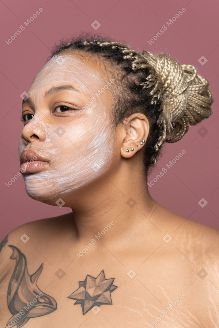 Frau mit einer kosmetischen maske auf ihrem gesicht, das transparenten spiegel betrachtet