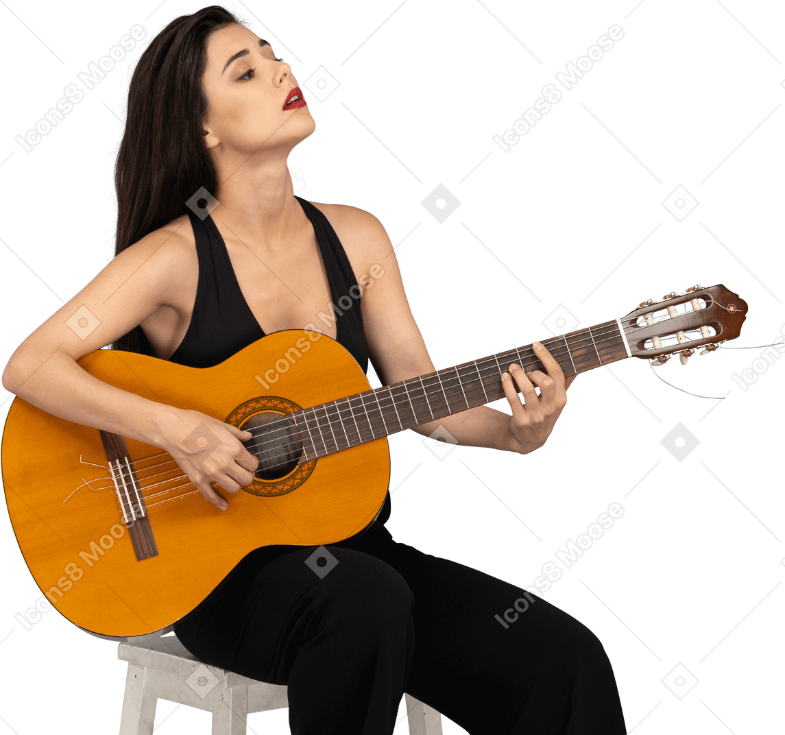 Three-quarter view of a sitting young lady in black suit holding the guitar and raising head