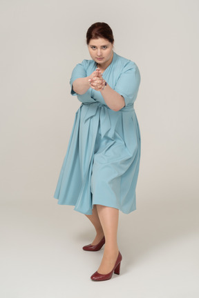 Vue de face d'une femme en robe bleue montrant un pistolet avec les doigts