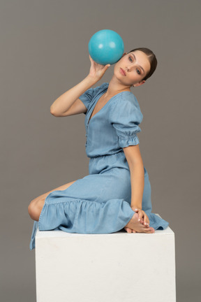 Side view of young woman sitting on a cube with ball on her head