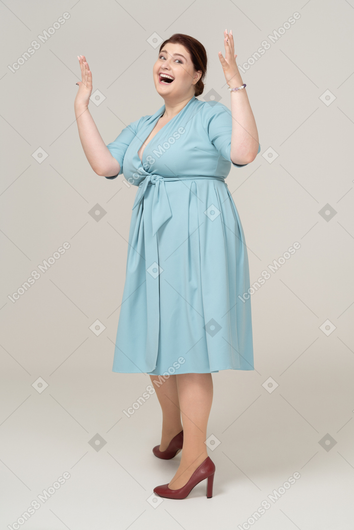 Front view of a happy woman in blue dress posing with raised arms